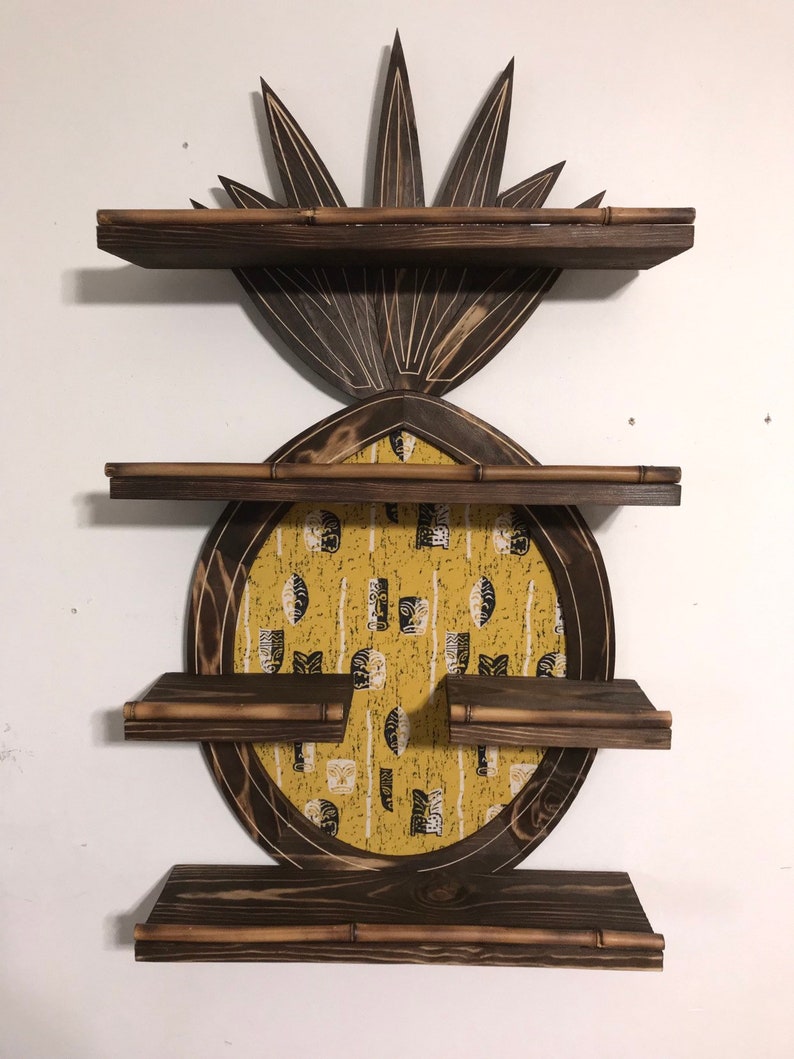 May include: A wooden pineapple-shaped shelf unit with three shelves. The shelves are made of dark wood with a light wood trim. The pineapple is decorated with a yellow and black patterned fabric.