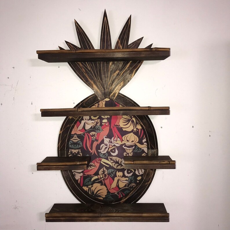 May include: A wooden pineapple-shaped shelf unit with three shelves. The pineapple is decorated with a colorful floral pattern and has a dark brown finish.