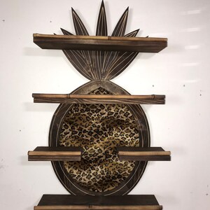 May include: A wooden pineapple-shaped shelf unit with three shelves. The shelves are made of dark brown wood and have a light brown trim. The pineapple is decorated with a leopard print fabric.