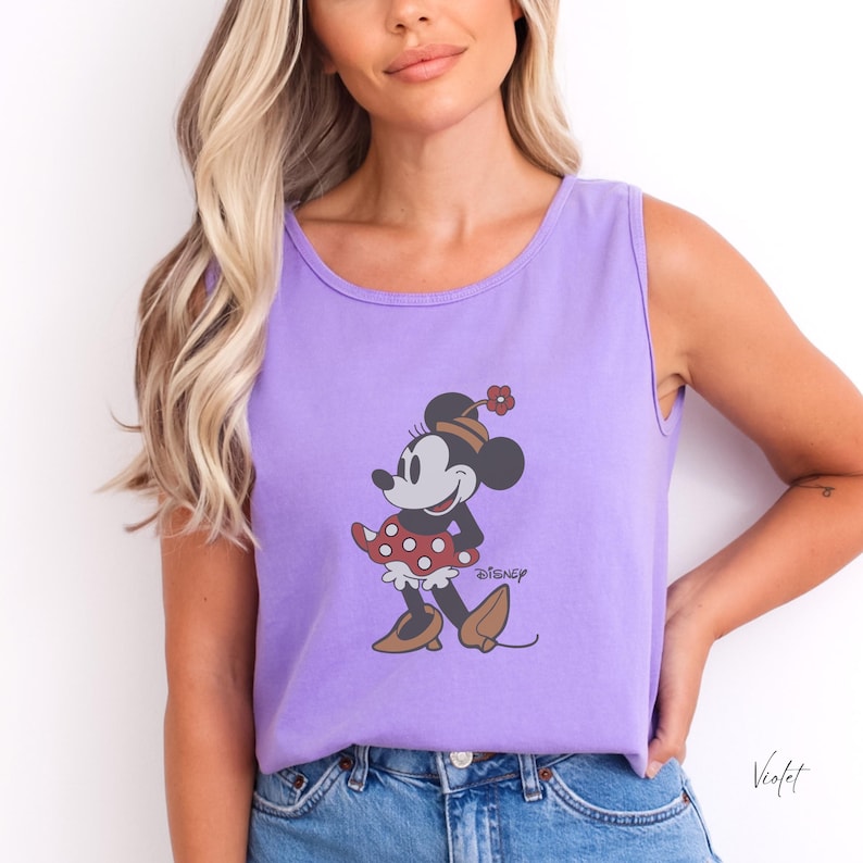 Peut inclure: Un d&eacute;bardeur violet avec un motif de Minnie Mouse. Le personnage de dessin anim&eacute; est repr&eacute;sent&eacute; avec une jupe &agrave; pois rouges, des chaussures marron et un chapeau assorti. Le mot "Disney" est imprim&eacute; en dessous.