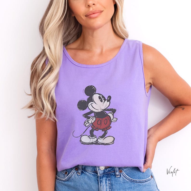 May include: A light purple sleeveless tank top featuring a centered graphic of Mickey Mouse. The character is depicted in a classic black and white style with red shorts, rendered with a distressed, vintage-inspired texture on the fabric.