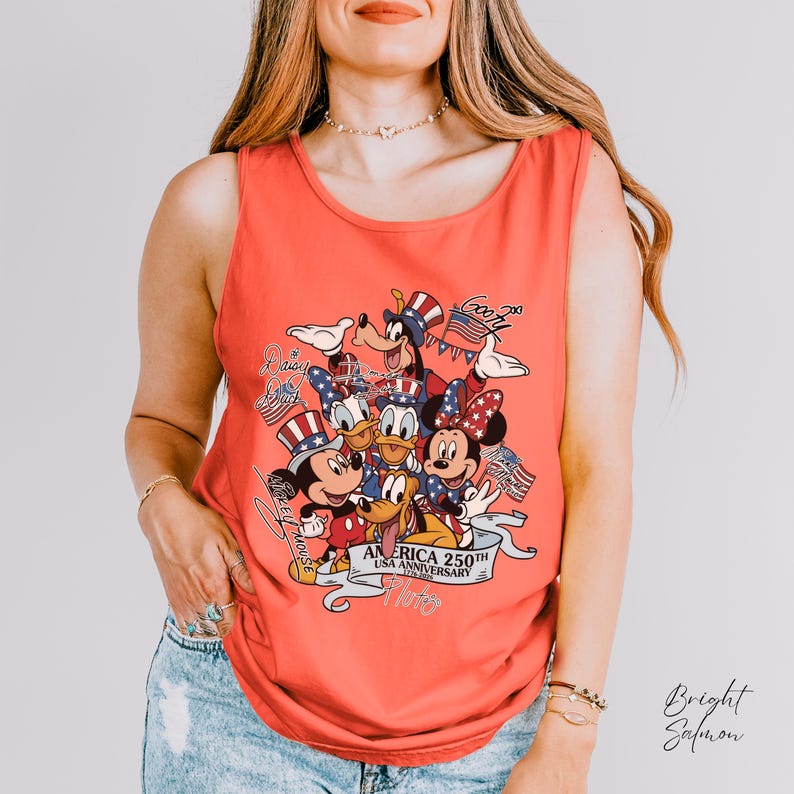 May include: A bright salmon sleeveless tank top featuring a graphic print of Disney characters including Mickey Mouse, Minnie Mouse, Donald Duck, Daisy Duck, Goofy, and Pluto wearing patriotic hats, with text reading America 250th USA Anniversary.