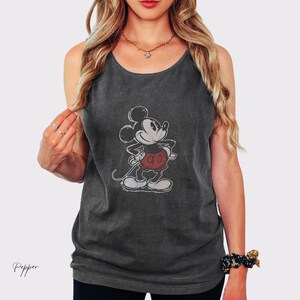 May include: A charcoal gray sleeveless tank top featuring a vintage-style graphic of Mickey Mouse in the center. The character is depicted in black and white with red shorts, standing with hands on hips. The fabric has a washed, textured appearance.