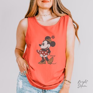 Peut inclure: D&eacute;bardeur corail avec un motif de Minnie Mouse. Le personnage de dessin anim&eacute; est repr&eacute;sent&eacute; dans une pose classique, portant une robe rouge &agrave; pois blancs et des chaussures marron. Le logo Disney est visible.
