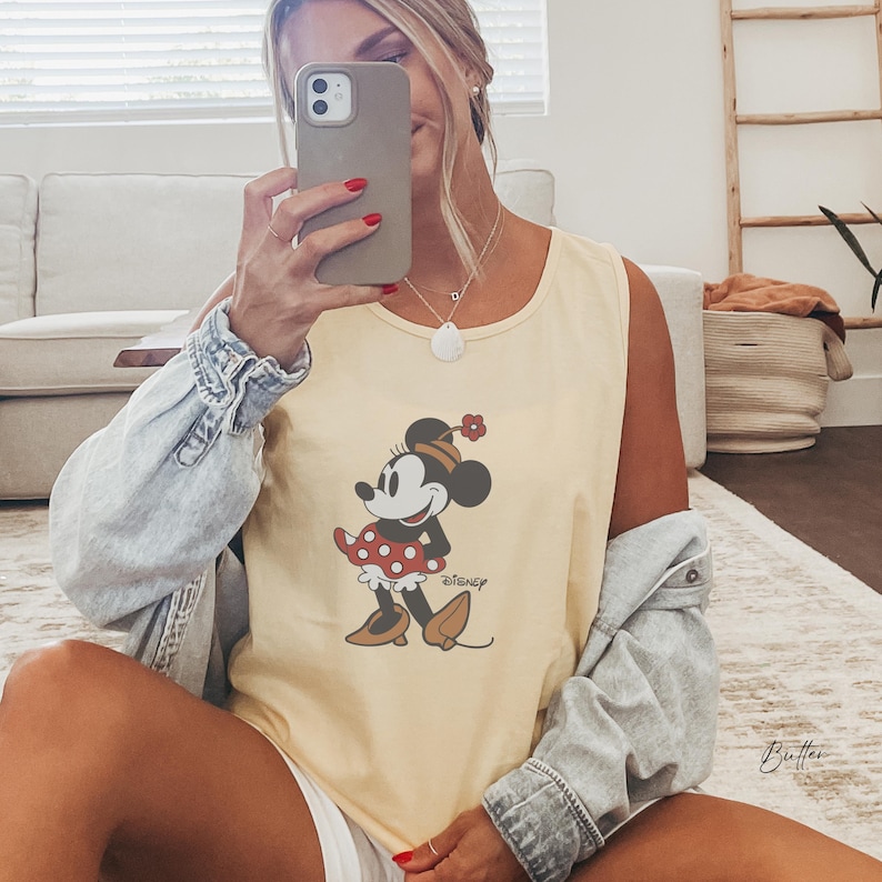 Peut inclure: Un d&eacute;bardeur jaune clair avec un motif de Minnie Mouse. La Minnie Mouse de dessin anim&eacute; porte une robe &agrave; pois rouges et blancs et un n&oelig;ud assorti. Le mot "Disney" est imprim&eacute; sous le motif.