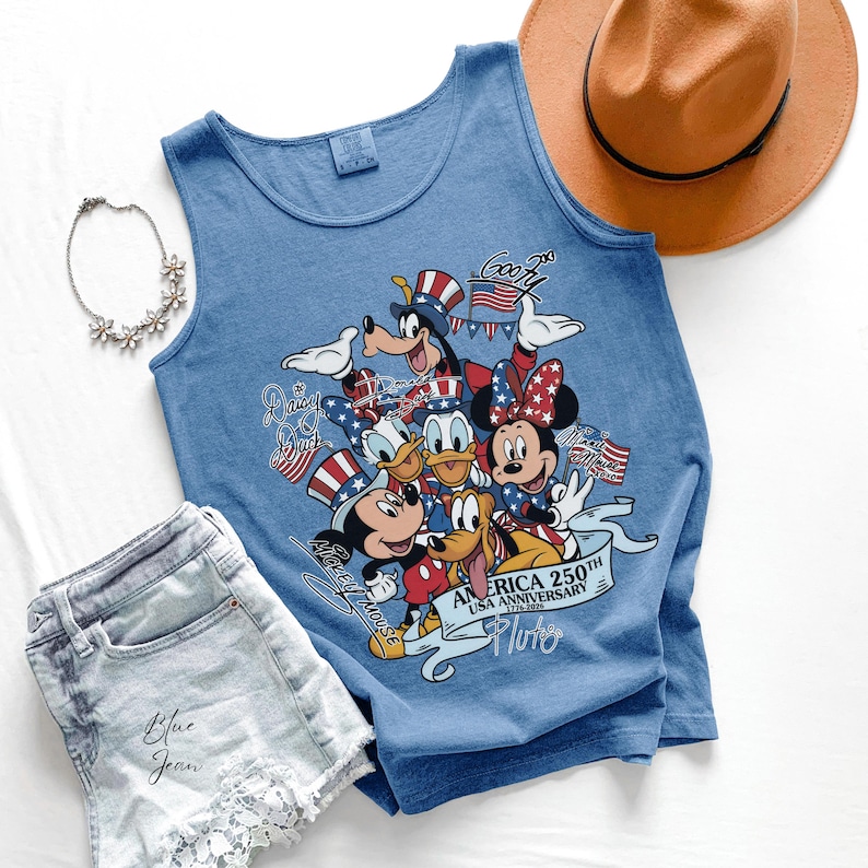 May include: A blue sleeveless tank top featuring a graphic print of Disney characters including Mickey Mouse, Minnie Mouse, Donald Duck, Daisy Duck, Goofy, and Pluto wearing patriotic hats. The text reads America 250th USA Anniversary 1776-2026.