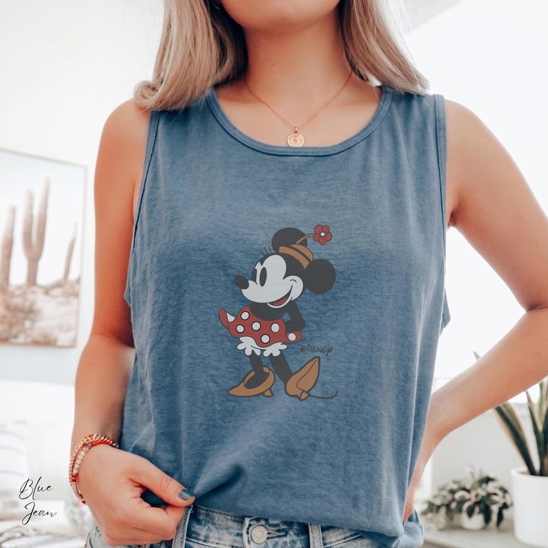 Peut inclure: Un d&eacute;bardeur bleu avec un motif de Minnie Mouse. La Minnie de dessin anim&eacute; porte une robe &agrave; pois rouges et blancs et un chapeau assorti avec une fleur. Le d&eacute;bardeur a une coupe d&eacute;contract&eacute;e et une esth&eacute;tique vintage.
