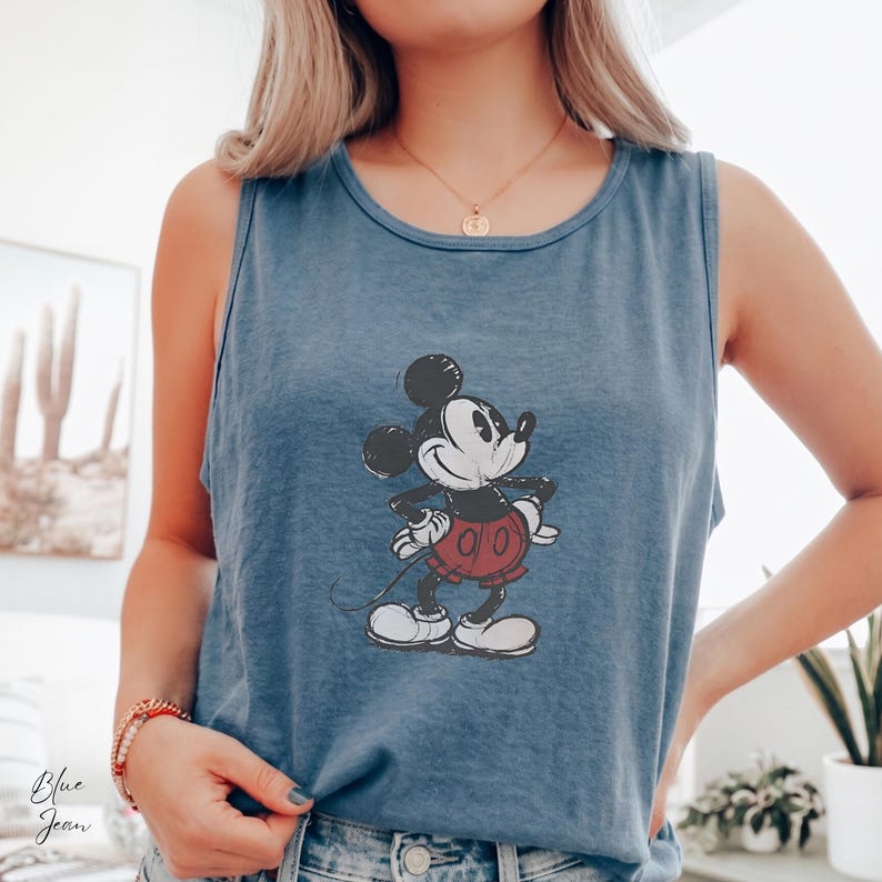 May include: A blue sleeveless tank top featuring a distressed graphic print of Mickey Mouse in the center. The character is depicted in a classic pose with black ears, a black body, red shorts, and white gloves and shoes, set against the blue fabric.