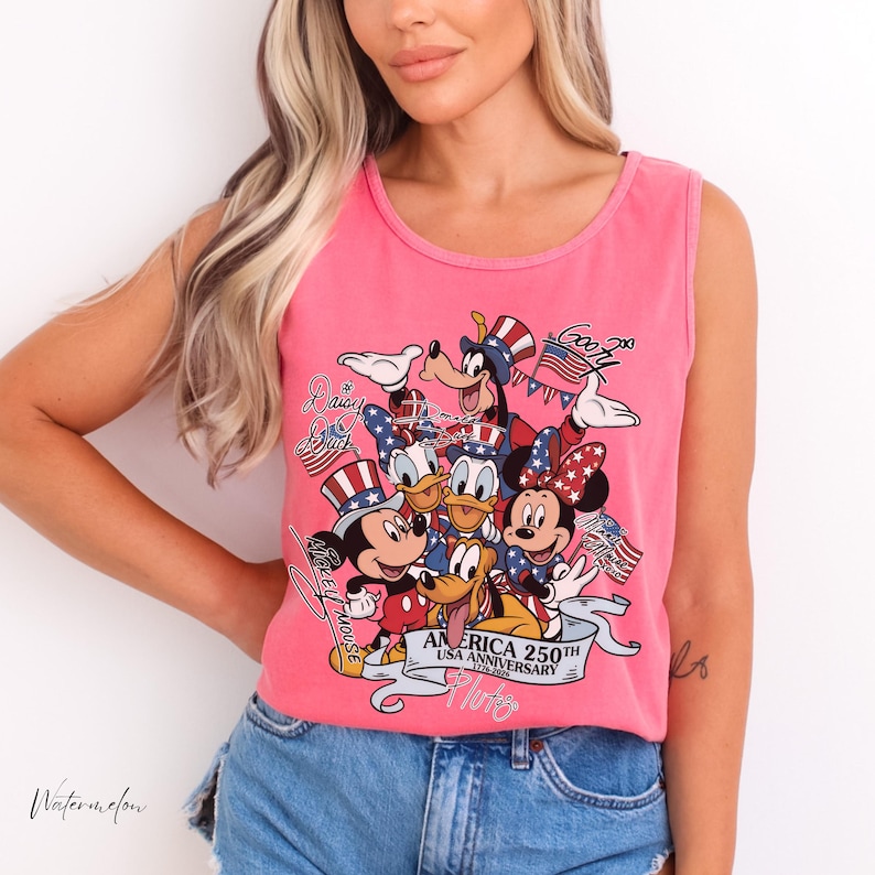 May include: A bright pink sleeveless tank top featuring a graphic print of various cartoon characters wearing patriotic red, white, and blue hats. The text reads "AMERICA 250TH USA ANNIVERSARY 1776-2026" along with names of the characters in script font.