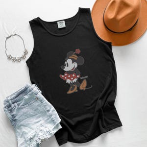 Peut inclure: D&eacute;bardeur noir avec un motif de Minnie Mouse. Le personnage de dessin anim&eacute; porte une robe &agrave; pois rouges et blancs, des chaussures marron et un chapeau avec une fleur. L'image comprend &eacute;galement un short en jean, un collier et un chapeau marron.