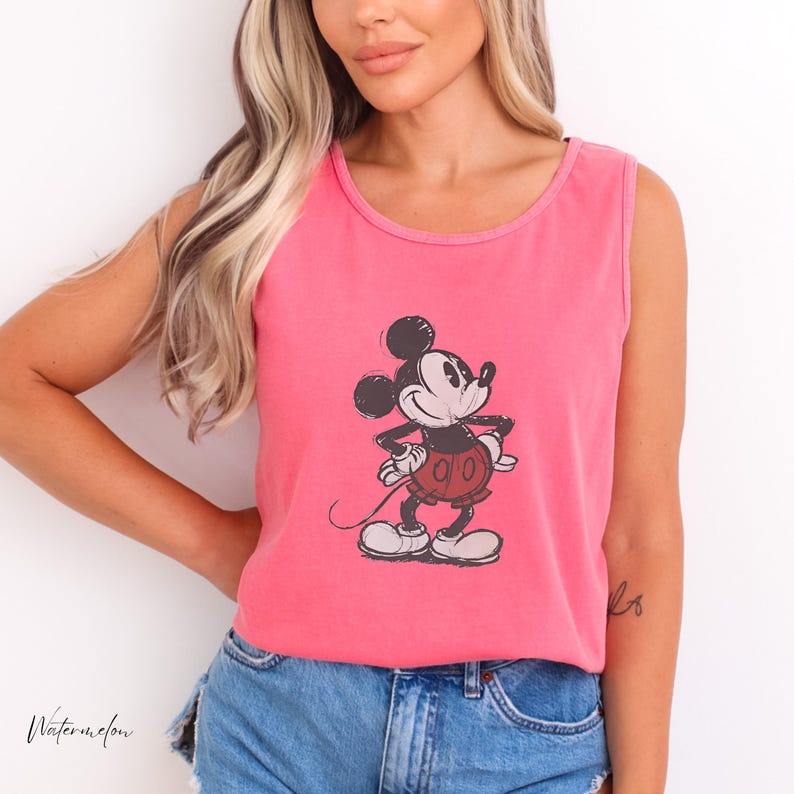 May include: A bright pink sleeveless tank top featuring a black and white graphic illustration of Mickey Mouse with red shorts. The character is depicted in a classic standing pose with hands on hips, centered on the front of the garment.
