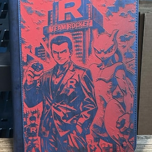 May include: A blue and red Team Rocket binder featuring a detailed graphic of a man, a Mewtwo-like creature, and the Team Rocket logo. The binder has a textured design and a dark blue spine.