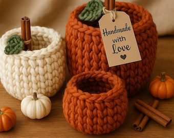 May include: A collection of handmade crochet pumpkin-shaped baskets in cream and orange, with green leaf accents and cinnamon stick stems. One basket has a tag that reads "Handmade with Love". Small pumpkins and cinnamon sticks are also present.