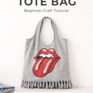 Peut inclure: Un sac fourre-tout gris fabriqué à partir d'un t-shirt, avec un motif de langue rouge et blanche. Le sac a une frange en bas et le texte "NO-SEW UPCYCLED T-SHIRT TOTE BAG Beginner Craft Tutorial".
