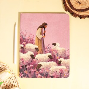 Peut inclure: Une housse de tablette rose avec une illustration d'un berger et de moutons dans un champ de fleurs roses. Le berger porte une longue robe beige et tient un bâton. Un stylet blanc est placé à côté de l'étui.