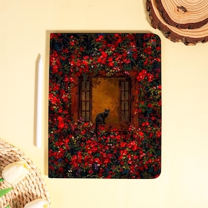 May include: A decorative tablet cover featuring a painting of a black cat in a window surrounded by red flowers. The artwork has a vintage aesthetic, with a warm color palette and detailed floral elements. A white stylus is placed to the left.