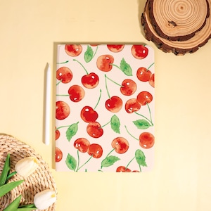 May include: A tablet case with a watercolor cherry pattern. The design features red cherries with green stems and leaves on a cream background. A white stylus rests beside the case. The case is rectangular.