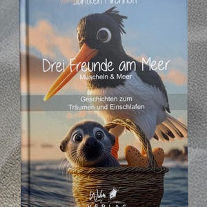 以下が含まれることがあります： 海鳥とアザラシがバスケットに入ったイラストが描かれた本の表紙。「Drei Freunde am Meer」というタイトルが大きく表示され、著者の名前と出版社のロゴも確認できます。テーマは、夢を見て眠りにつくための物語です。