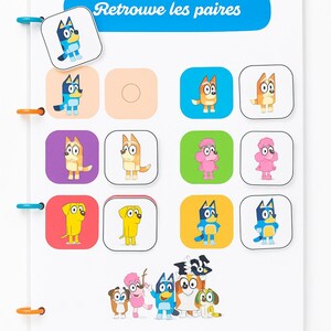 May include: A white activity board with colorful cartoon dog characters. The board has a blue banner with the text "Retrouve les paires". The board has a matching game with colorful squares and cartoon dog characters.