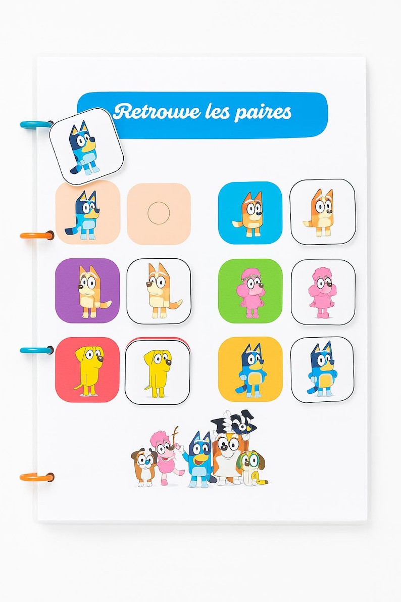 May include: A white activity board with colorful cartoon dog characters. The board has a blue banner with the text "Retrouve les paires". The board has a matching game with colorful squares and cartoon dog characters.