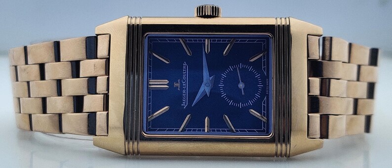 May include: A gold-toned rectangular wristwatch with a navy blue face. The watch features a small seconds dial and gold-toned hands and markers. The watch band is made of gold-toned rectangular links.