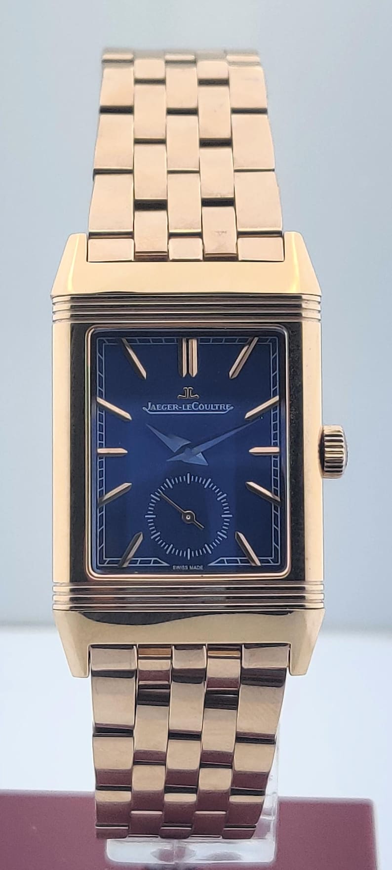 May include: A gold-toned rectangular wristwatch with a blue face. The watch features the brand name "JAEGER-LECOULTRE" and "SWISS MADE" text. The watch band is also gold-toned.