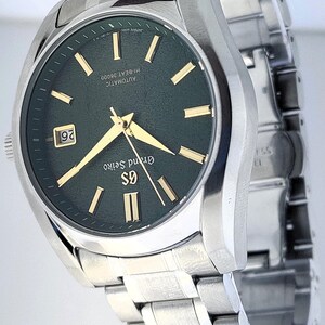 May include: A stainless steel wristwatch with a dark green face and gold-colored hands and markers. The watch has a date display at the 3 o'clock position and a silver-colored band. The watch face has the text "Grand Seiko" and "AUTOMATIC HI-BEAT 36000".