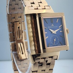May include: A gold-toned wristwatch with a rectangular blue face and gold hands. The watch features a gold band with a woven design. The watch face has the text "JAEGER-LECOULTRE".