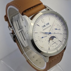 May include: A silver-toned Jaeger-LeCoultre watch with a white face and brown leather band. The watch face displays multiple subdials, the date, and the text "FOR 30 PULSATIONS". The band is light brown.