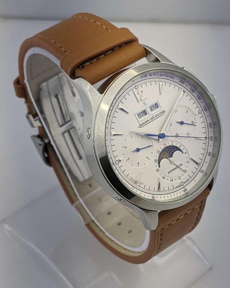 May include: A silver-toned Jaeger-LeCoultre watch with a white face and brown leather band. The watch face displays multiple subdials, the date, and the text "FOR 30 PULSATIONS". The band is light brown.