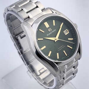 May include: A stainless steel wristwatch with a dark green face and gold-colored hands and markers. The watch has a date display at the 3 o'clock position and a metal band. The watch face has the text "Grand Seiko" and "Automatic Hi-Beat 36000".