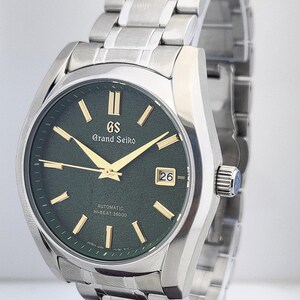 May include: A stainless steel Grand Seiko automatic watch with a dark green dial. The watch features gold-colored hands and markers, a date window at the 3 o'clock position, and the text "Grand Seiko" and "Automatic Hi-Beat 36000".