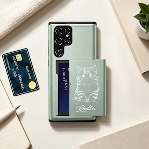 May include: A light green smartphone case with a sliding card holder compartment. The sliding panel features a white line drawing of a kitten and the name Bella printed below it. A dark blue credit card is partially inserted into the holder.