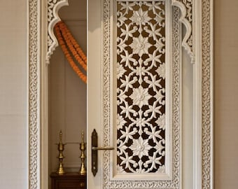 May include: Ornate white wooden door with intricate floral carvings. The door features a decorative frame and a central panel with a lattice design. The door is partially open, revealing a glimpse of the interior with gold accents and orange flowers.