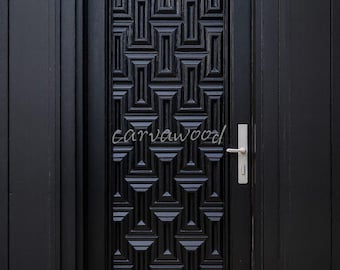 May include: A black wooden door with a geometric pattern and a silver handle. The door is set in a black frame and features the text "carvawood". The door is surrounded by black siding.