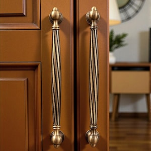 May include: Two antique bronze cabinet pulls with a spiral design. The pulls have a decorative top and bottom, and are mounted on a brown cabinet door. The image includes the text "Hookzcrafts".