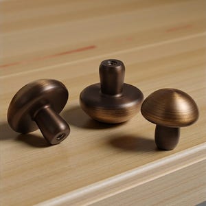 Puede incluir: Tres tiradores de armario con forma de hongo de bronce. Los tiradores tienen un acabado vintage y antiguo. Los sombreros de los hongos son redondeados y los tallos son cilíndricos. Los tiradores están diseñados para muebles y añaden un toque decorativo.