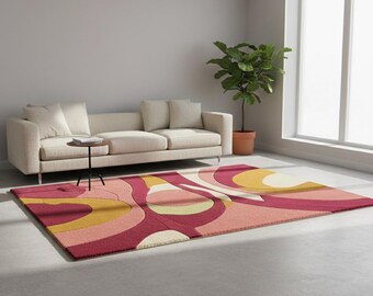 以下が含まれることがあります： ピンク、赤、黄色、クリーム色のレトロなデザインの長方形のラグ。 ラグは渦巻く抽象的なパターンが特徴で、リビングルームのコンクリートの床に置かれています。