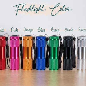 Puede incluir: Una colecci&oacute;n de peque&ntilde;as linternas cil&iacute;ndricas en varios colores: rojo, rosa, naranja, azul, verde, negro y plateado. Cada linterna tiene un cuerpo texturizado, una correa de mu&ntilde;eca negra y el texto "Flashlight Color" arriba.