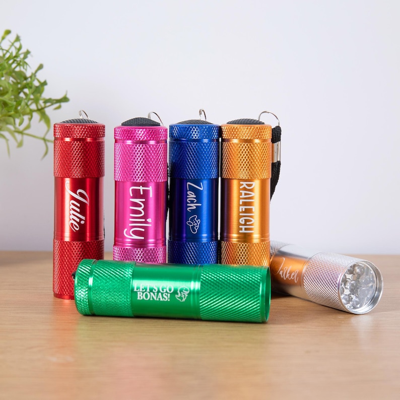 Puede incluir: Un conjunto de linternas de colores rojo, rosa, azul, naranja, verde y plateado. Cada linterna est&aacute; grabada con un nombre, como "Julie", o una frase como "Let's Go Bonas!"