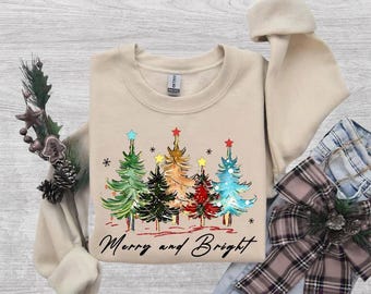 May include: A beige crewneck sweatshirt featuring a graphic of five stylized Christmas trees in green, dark green, gold, red, and blue, topped with stars. The text "Merry and Bright" is printed in black cursive script below the trees.