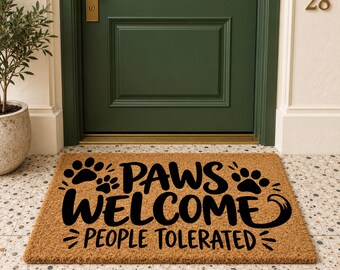 May include: A rectangular tan coir doormat featuring black text that reads PAWS WELCOME PEOPLE TOLERATED. The design includes black paw print graphics and decorative flourishes surrounding the lettering on the textured natural fiber surface.