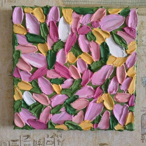 Puede incluir: Arte en lienzo cuadrado con un diseño floral texturizado. La obra presenta un fondo verde con pinceladas superpuestas en tonos de rosa, amarillo, blanco y verde, creando un efecto tridimensional. La pintura está enmarcada con un borde verde.