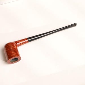 Könnte beinhalten: Eine Tabakpfeife mit einem rotbraunen Kopf und einem langen, schwarzen Stiel. Der Kopf hat ein Holzmaserungsmuster. Die Pfeife ist abgewinkelt und scheint aus Holz und einem schwarzen Material gefertigt zu sein. Die Pfeife befindet sich auf weißem Hintergrund.