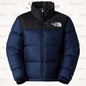 Puede incluir: Chaqueta acolchada azul marino y negra con cuello alto y cremallera completa. El logotipo blanco "THE NORTH FACE" está en el pecho. Diseñada para brindar calidez y protección contra los elementos.