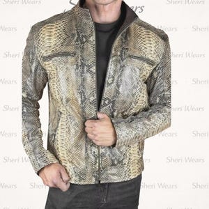 Könnte beinhalten: Jacke mit Schlangenmuster, Reißverschluss und zwei Brusttaschen. Die Jacke hat einen Stehkragen und ist in den Farbtönen Beige, Braun und Grau gehalten. Der Text "Sheri Wears" ist im Hintergrund sichtbar.