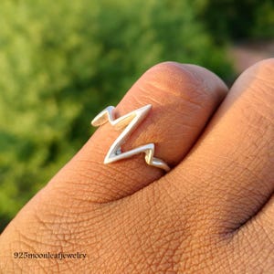 Puede incluir: Un anillo de plata con un diseño en zigzag. El anillo está hecho de un metal brillante y se lleva en un dedo. El diseño del anillo se asemeja a una cordillera estilizada. El texto "925moonleafjewelry" es visible en la parte inferior de la imagen.