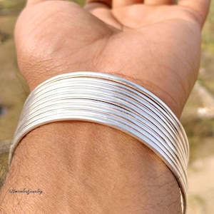 Könnte beinhalten: Ein Stapel silberner Armreifen an einem Handgelenk. Die Armreifen sind dünn und glänzend und reflektieren das Licht. Der Schmuck wird an einem Arm getragen. Der Text "925moonleafjewelry" ist unten im Bild zu sehen.