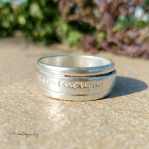 Peut inclure: Une bague en argent avec l'inscription "I am enough" gravée sur le bandeau. La bague a un design simple et élégant, avec une finition lisse et polie. C'est un bijou.