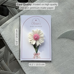 May include: A white card with a pink daisy embellishment, measuring 14.8 cm by 10.5 cm. The card reads "Rosie's BABY SHOWER" and includes the text "Thank You For Joining Us". The card is printed on 250 gsm premium matte paper.